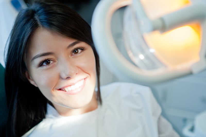 Asian American woman shows off her bright smile sitting in a dental chair ready for her cleaning