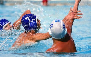 Three men competing in an aggressive game of water polo. The nature of the game creates numerous fast-moving arm swings, usually over the head, which increases the potential for head injury.