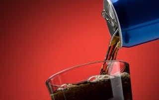 A blue can of a sugary soda being poured into a drinking glass with ice. Even though we aren’t sure about the link between sugary beverages and cancer, we do know that these beverages are not good for your teeth.