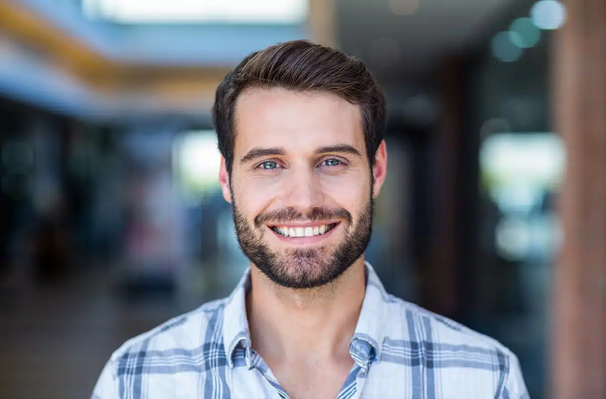 Man with short brown beard wearing a blue flannel shirt, highlighting his enhanced smile