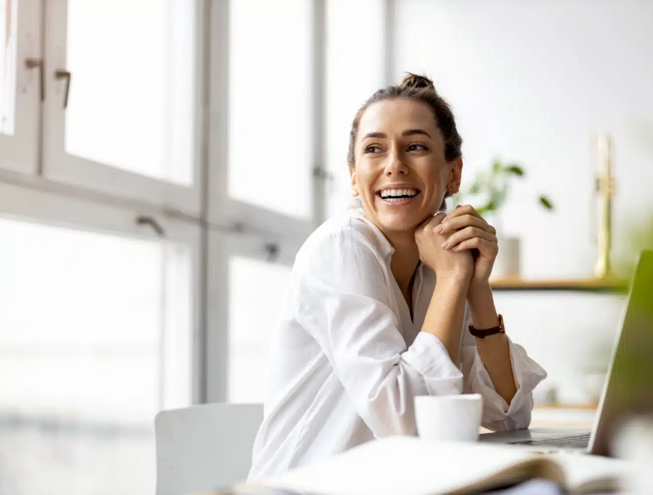 Professional office woman in a white blouse, sitting at a computer, laughing with a happy smile