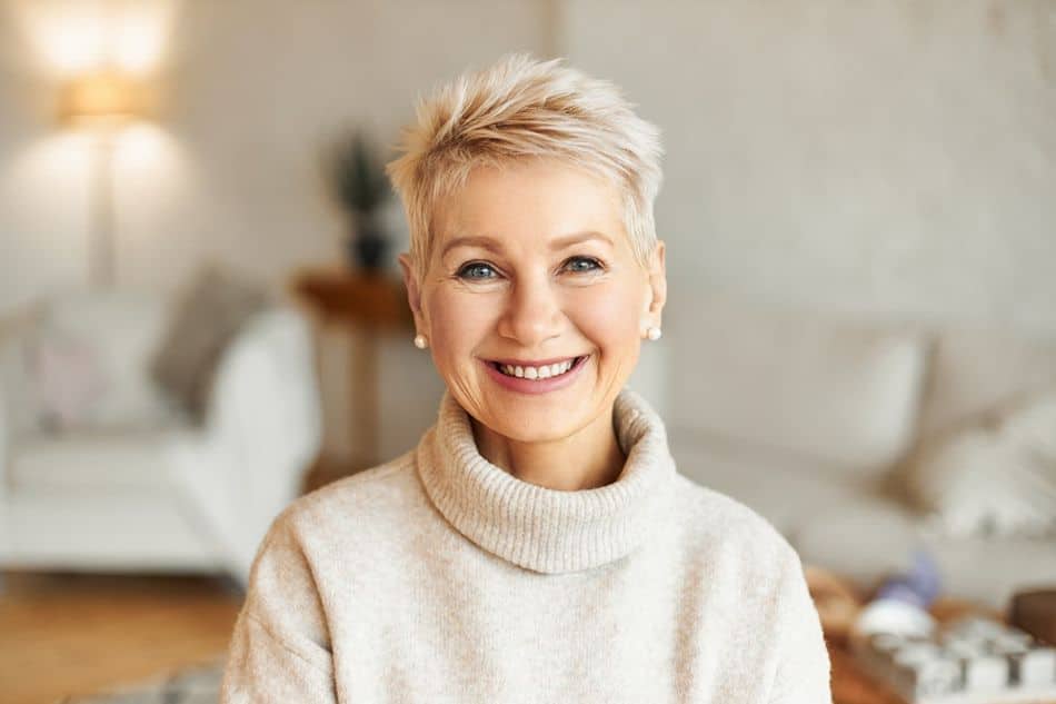 A mature woman with short, blonde hair wearing a white sweater smiling